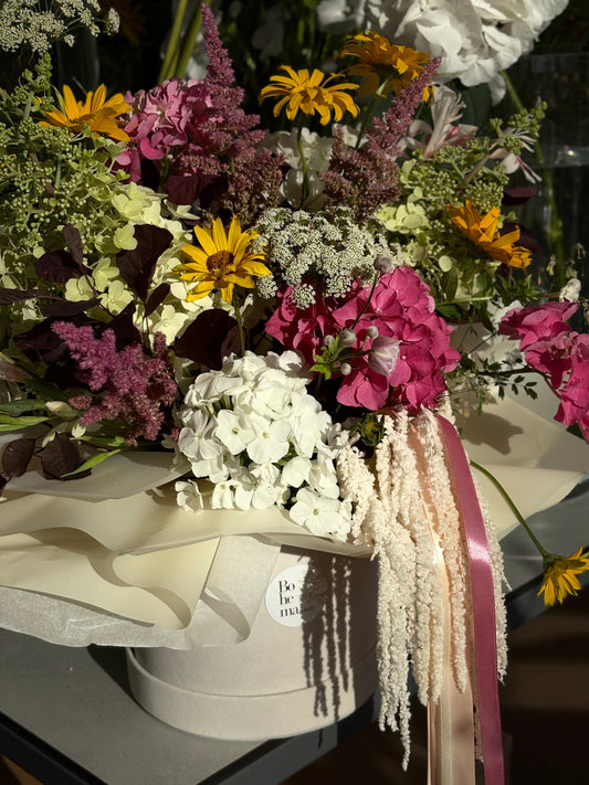 Šviesių pavasarinių spalvų gėlių kompozicija dėžutėje su baltais, gelsvais ir rausvais atspalviais, natūrali, laisvos formos struktūra