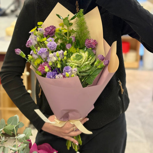 Violetinių tonų gėlių puokštė su įvairiais violetiniais, alyviniais ir žalsvais atspalviais, subalansuota, vidutinio tankumo kompozicija
